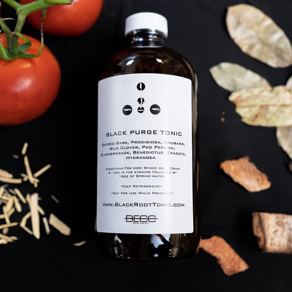 A bottle of Black Purge Tonic with tomatoes, dried leaves, and wood shavings on a dark surface.