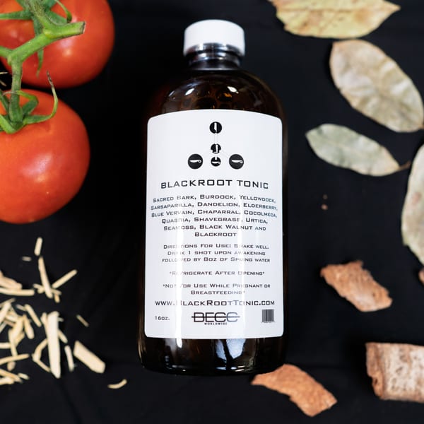 A bottle of Blackroot Tonic with tomatoes, wood shavings, and dried leaves on a black surface.