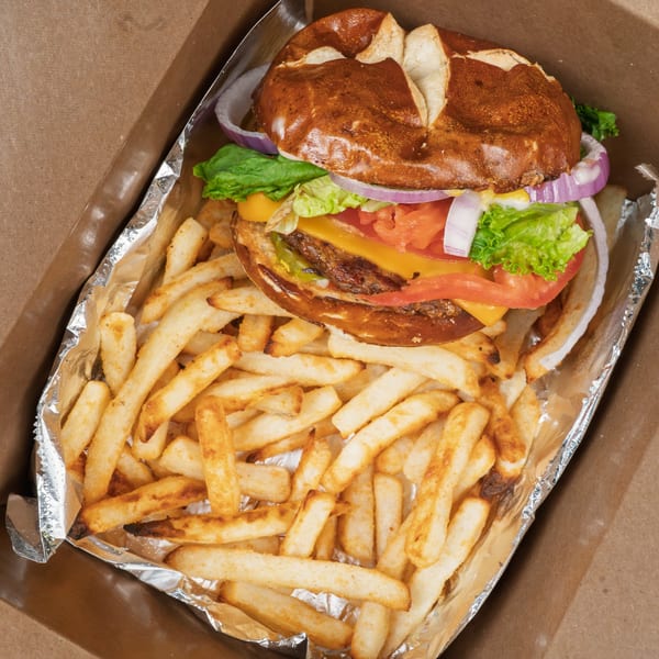 Vegan burger with lettuce, tomato, onion, and cheese on a pretzel bun, with fries.